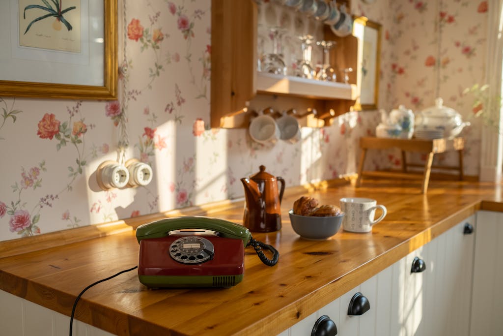 A beautifully lit retro kitchen featuring a vintage rotary phone and floral wallpaper.